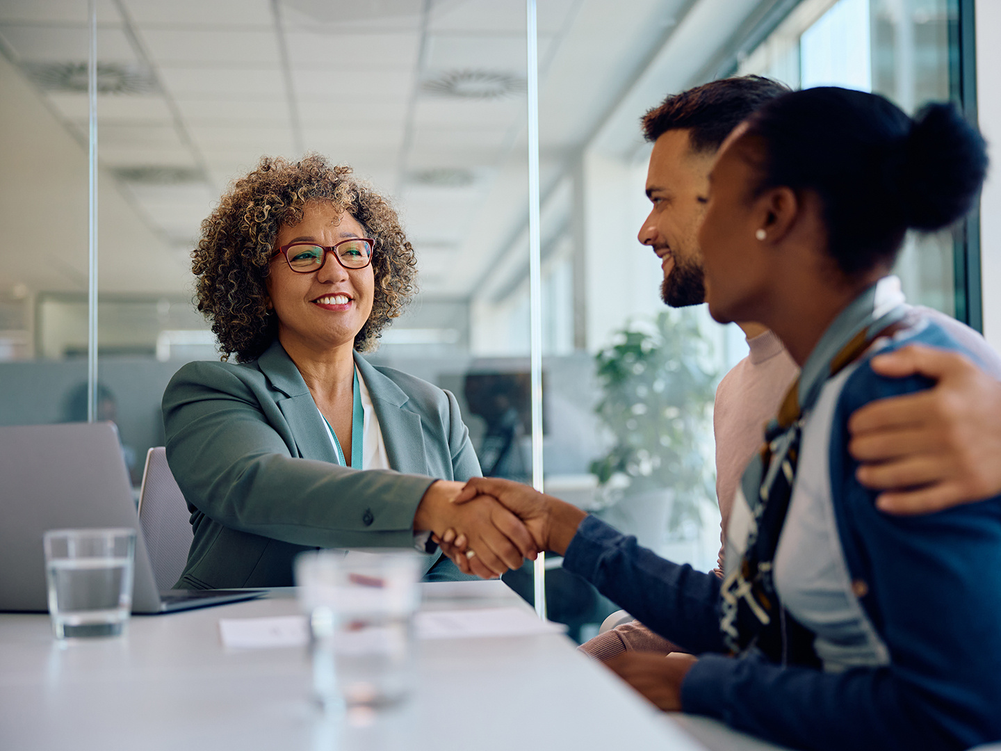 Happy insurance agent and young couple shaking hands after successful deal during a meeting in the office.